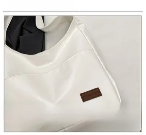 Close-up of minimalist white PU leather tote bag with brown leather brand tag detail