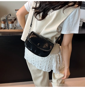 Detail of glossy black patent leather saddle bag with round snap button and slim strap