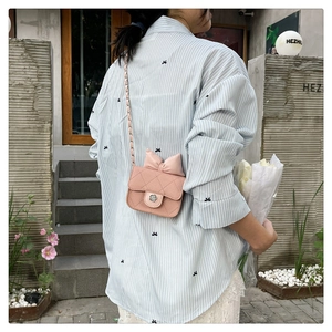 Pink quilted square crossbody bag with decorative bow and metal chain strap shown on model