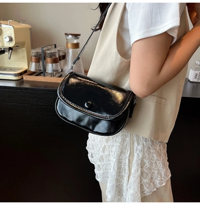 Glossy black PU leather crossbody bag with a magnetic snap closure shown in a cafe