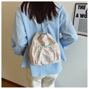 Rear view of a floral drawstring tote bag with a blue plaid bow on a model back