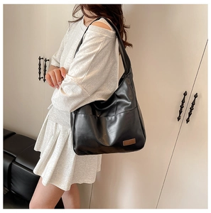 Detail of black large-capacity tote bag in soft faux leather with fashion brand label