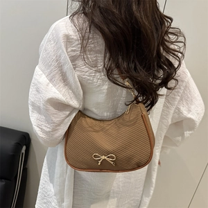 Brown woven half-moon underarm bag with gold bow detail worn by a model