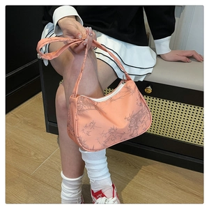 Detailed view of peach pink underarm bag with bamboo pattern on seated model indoors