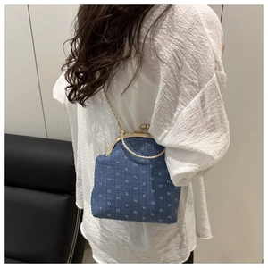 Detail of dark blue denim crossbody bag with gold clasp and chain strap on a model