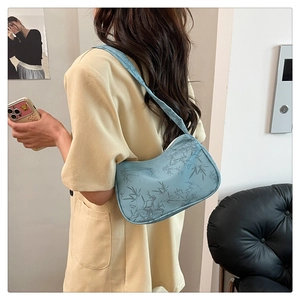 Detail view of light blue underarm bag with grey bamboo leaf print on model's shoulder