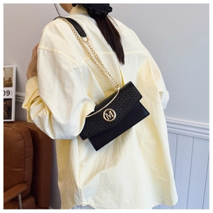 Detail of black patchwork shoulder bag with woven flap and golden M logo on model