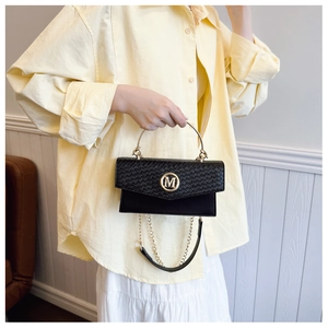 Detail of woven texture flap with gold M logo on a black leather crossbody handbag
