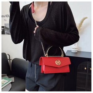 Detail of red woven texture flap bag with gold M logo and chain strap on a model