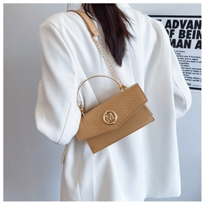 Detail of tan textured handbag with gold M logo and chain strap on white blazer