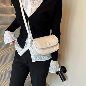 Minimalist beige crossbody bag with semi-circular flap shown on a model in a clean setting