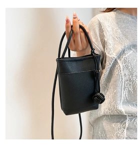 Detail of black mini bucket bag with lychee texture leather and woven ball charm