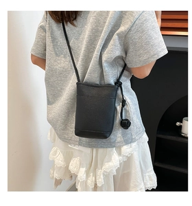 Detail of black pebbled leather mini crossbody bag with side woven ball charm