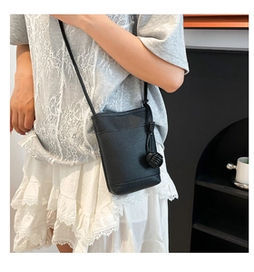 Detail of black mini bucket bag featuring lychee texture and woven ball pendant charm