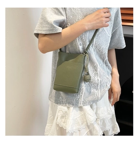 Detail of avocado green leather crossbody phone bag with woven ball charm on a model
