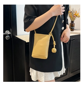 Detail of yellow lychee texture leather mini crossbody bag with decorative knot and ball