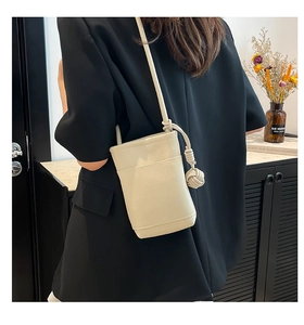 Detail view of beige bucket bag with lychee texture and decorative knot strap on a model