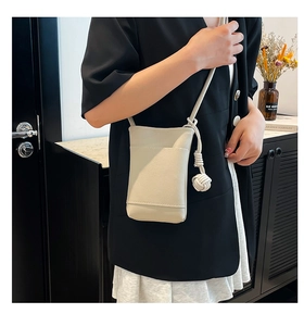 Detail view of cream lychee leather crossbody phone bag with woven knot charm decoration