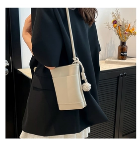 Close-up of ivory leather mini crossbody bag with ball knot charm on a black blazer