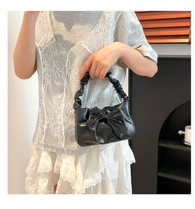 Detail of black pleated handle handbag with large bow and elegant metal chain strap