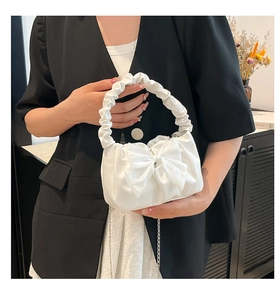 Detail of white satin handbag featuring a chic bow and ruffled cloud handle with chain