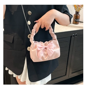 Detail of light pink satin handbag with large bow and ruffled handle held by a model