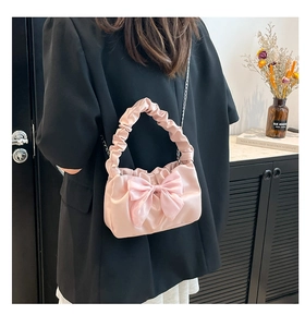 Detailed view of pink satin handbag featuring a large bow and elegant metal chain strap