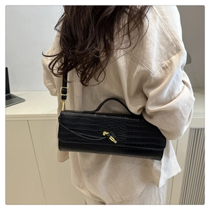 Crocodile pattern baguette bag with gold buckle on shoulder of a model in beige suit