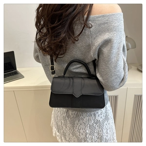 Minimalist black leather crossbody bag shown on model in a modern office setting