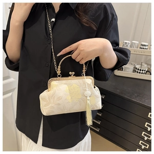 Detailed close-up of floral embroidery on cream shell bag with metallic gold handle and tassel