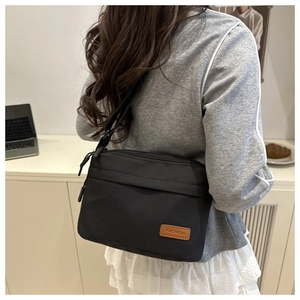 Détail du sac bandoulière en nylon noir avec poches zippées et écusson tendance