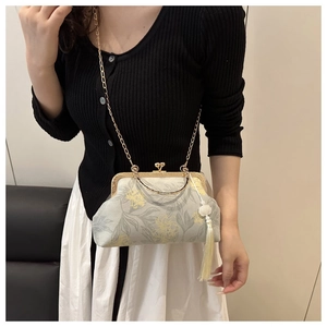 Detail of floral frame bag with gold chain and yellow tassel charm on grey fabric