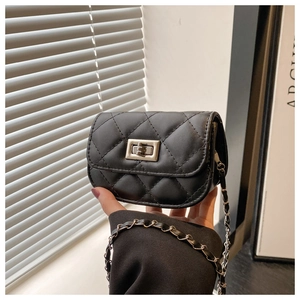 Detail of a black quilted mini crossbody bag with silver clasp and chain strap held by hand
