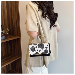 Detalle de bolso con estampado de vaca, asa dorada y correa de cadena en modelo