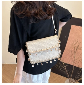Detail of straw crossbody bag with shell pendants on a model in a minimal studio