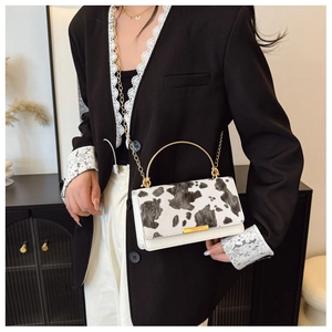 Close-up of cow print crossbody bag with gold handle and chain on model in black suit