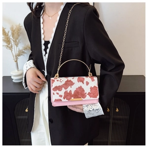 Close-up of pink cow pattern crossbody bag with gold handle and chain shoulder strap
