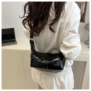 Glänzende schwarze Schultertasche in Halbmondform mit Ziernähten im modernen Büro-Ambiente