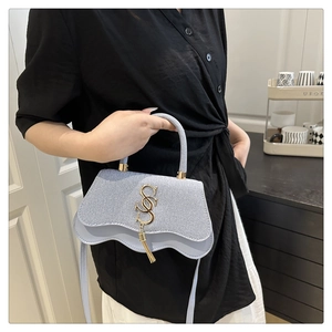 Detail of light blue crossbody bag with wavy flap and golden S-letter charm detail