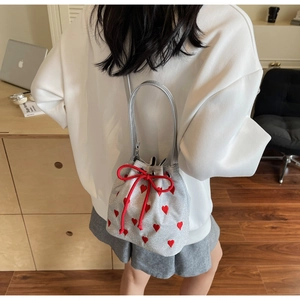 Silver bucket bag with red heart pattern shown as a crossbody on a casual outfit