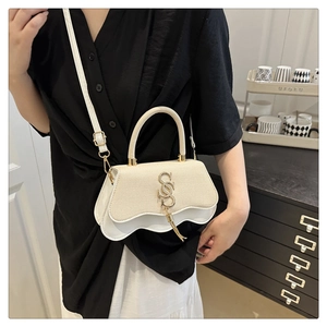 Close-up of stylish cream handbag with wavy base, woven texture, and gold S-shaped hardware