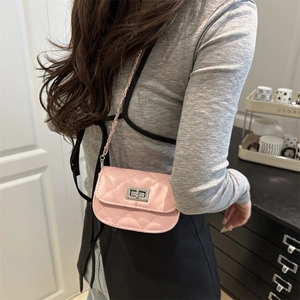 Pink quilted mini saddle bag with silver chain strap worn by a model in a minimal room