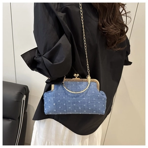 Detail of denim blue shell bag with gold chain strap and vintage clasp worn by model
