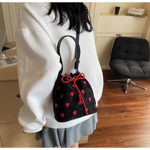 Rear view of a black canvas bucket bag with red heart embroidery and bow drawstring