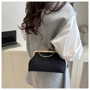 Detail of black flocking shell bag with gold handle and chain worn by a model