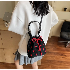 Mini black bucket bag with red heart embroidery and drawstring bow worn by a model