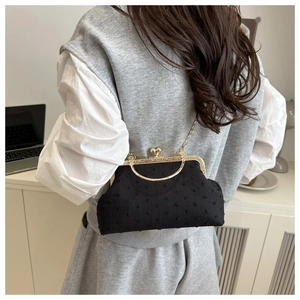 Detail of black shell crossbody bag with polka dot texture and gold clasp on a model