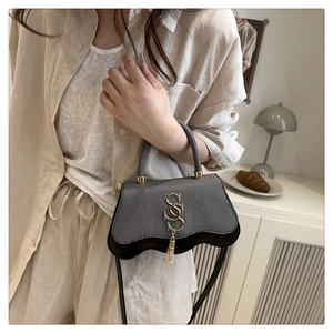 Close-up of wavy base and gold SS logo with tassel on woven leather handbag