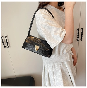 Detail view of black crocodile pattern shoulder bag with a gold round buckle on a model
