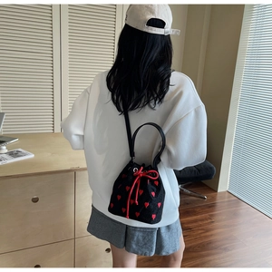 Detail of black canvas bucket bag featuring red heart embroidery and drawstring closure